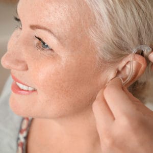 Doctor inserting hearing aid in ear of mature woman, closeup